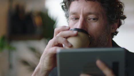 attractive caucasian businessman in cafe using tablet computer watching online entertainment reading social media messages enjoying drinking coffee relaxing