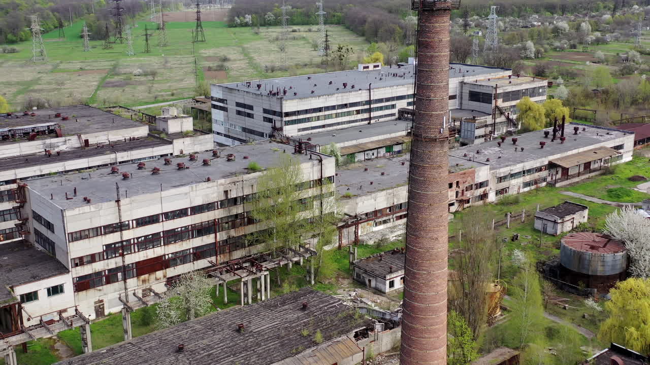 Panoramic view of an old factory. Abandoned territory of industrial plant with large brick pipe. Ruined manufacting in springtime. Aerial view.
