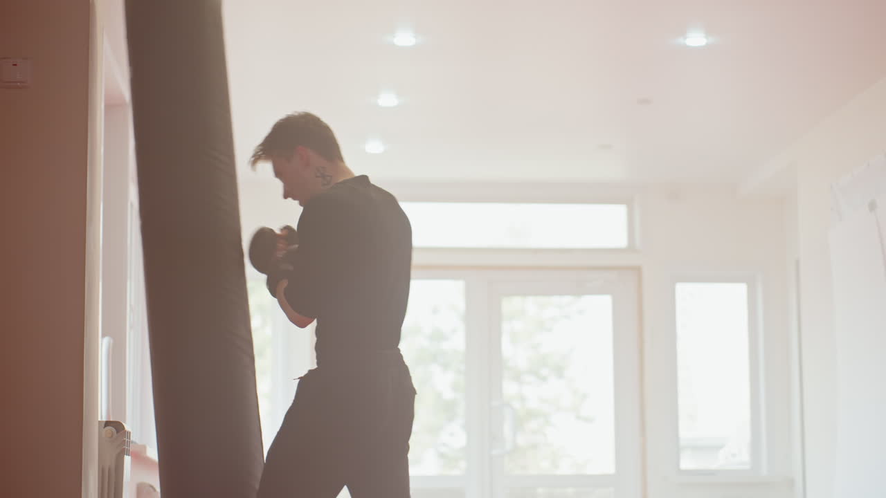 Athlete wearing gloves practices boxing strikes on punching bag inside bright gym, showcasing focus, power, discipline, stamina, and training intensity during martial arts workout emphasizing precision