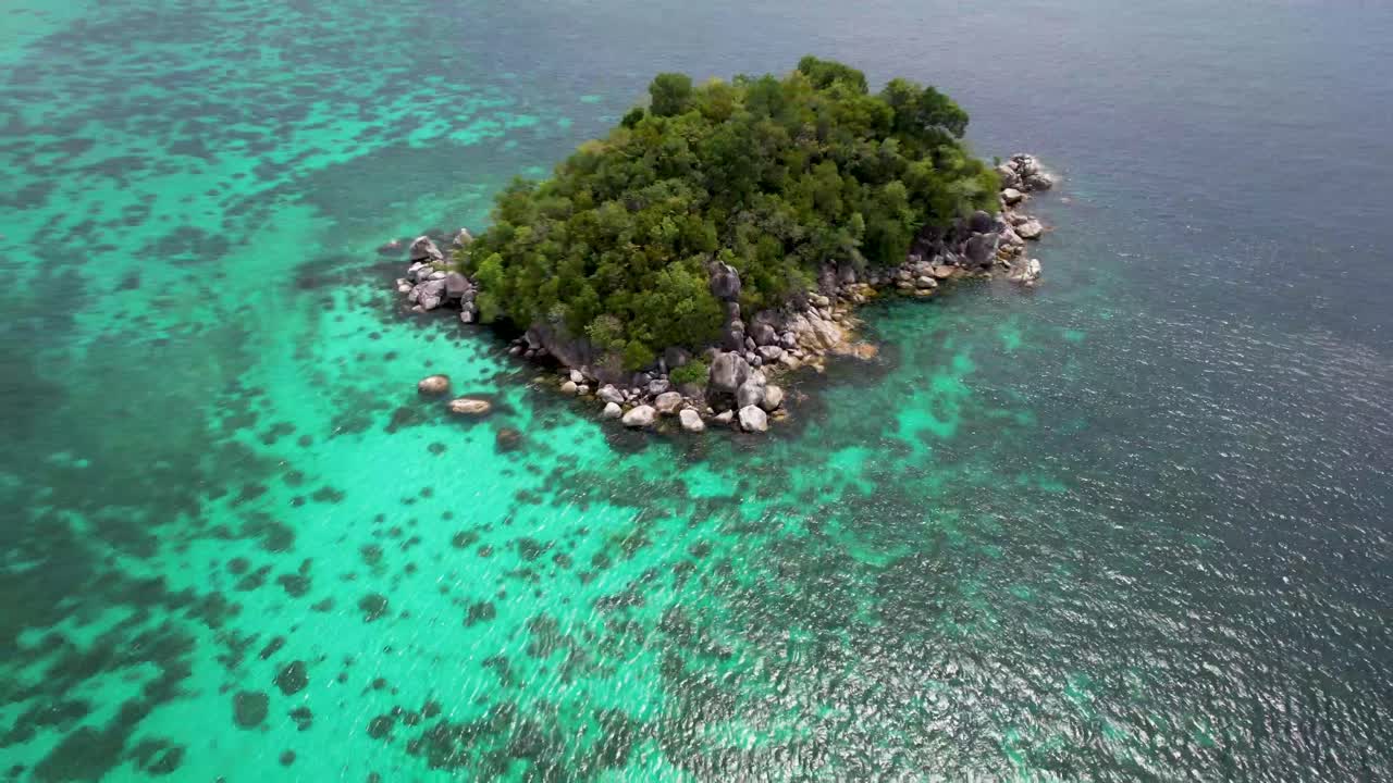 Small uninhabited Tropical Island surrounded by coral reefs with one boat anchored off shore- aerial pull back