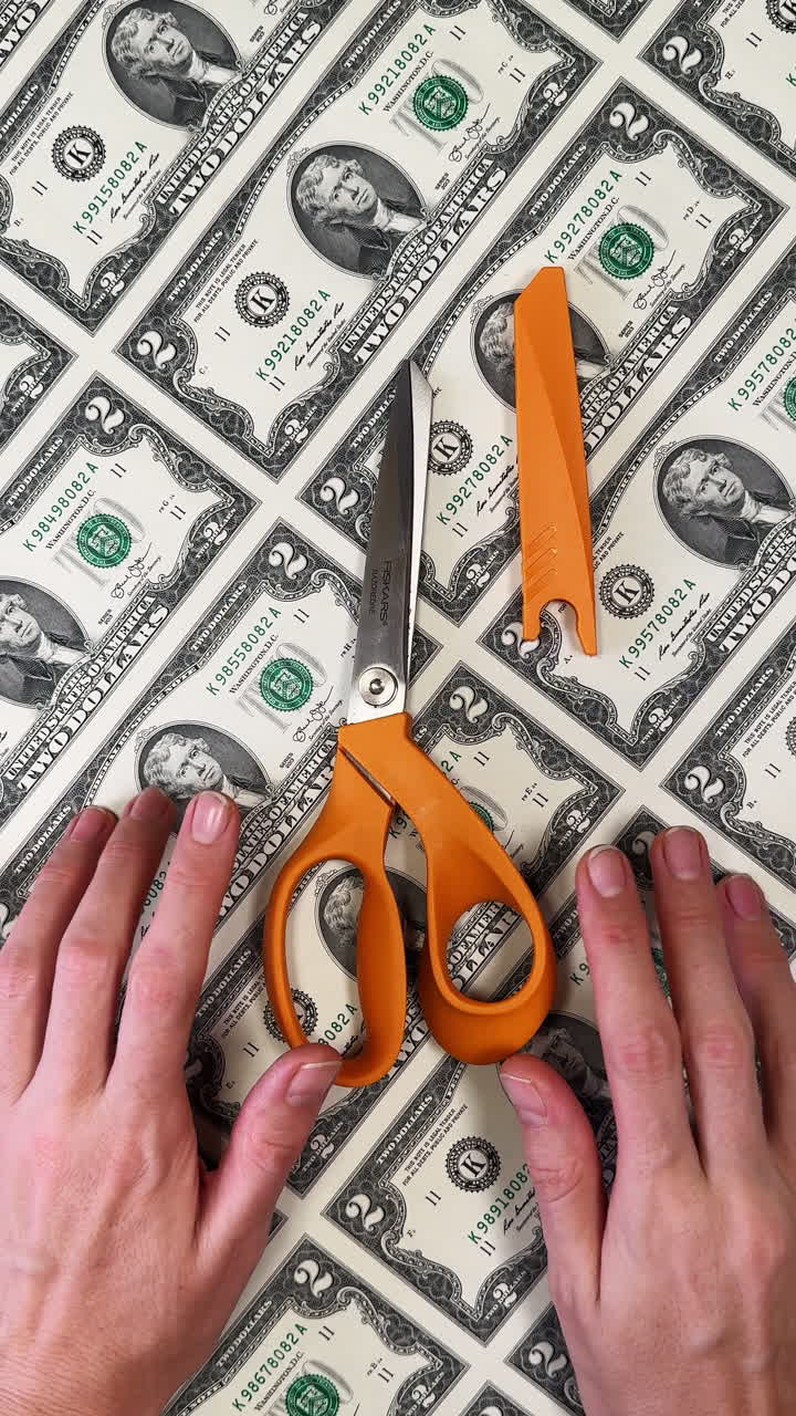 San Antonio, USA, 14 August 2025: Scissors with orange handles and female hands placed on the uncut sheet of American two dollar banknotes. Finance and money printing. Vertical video