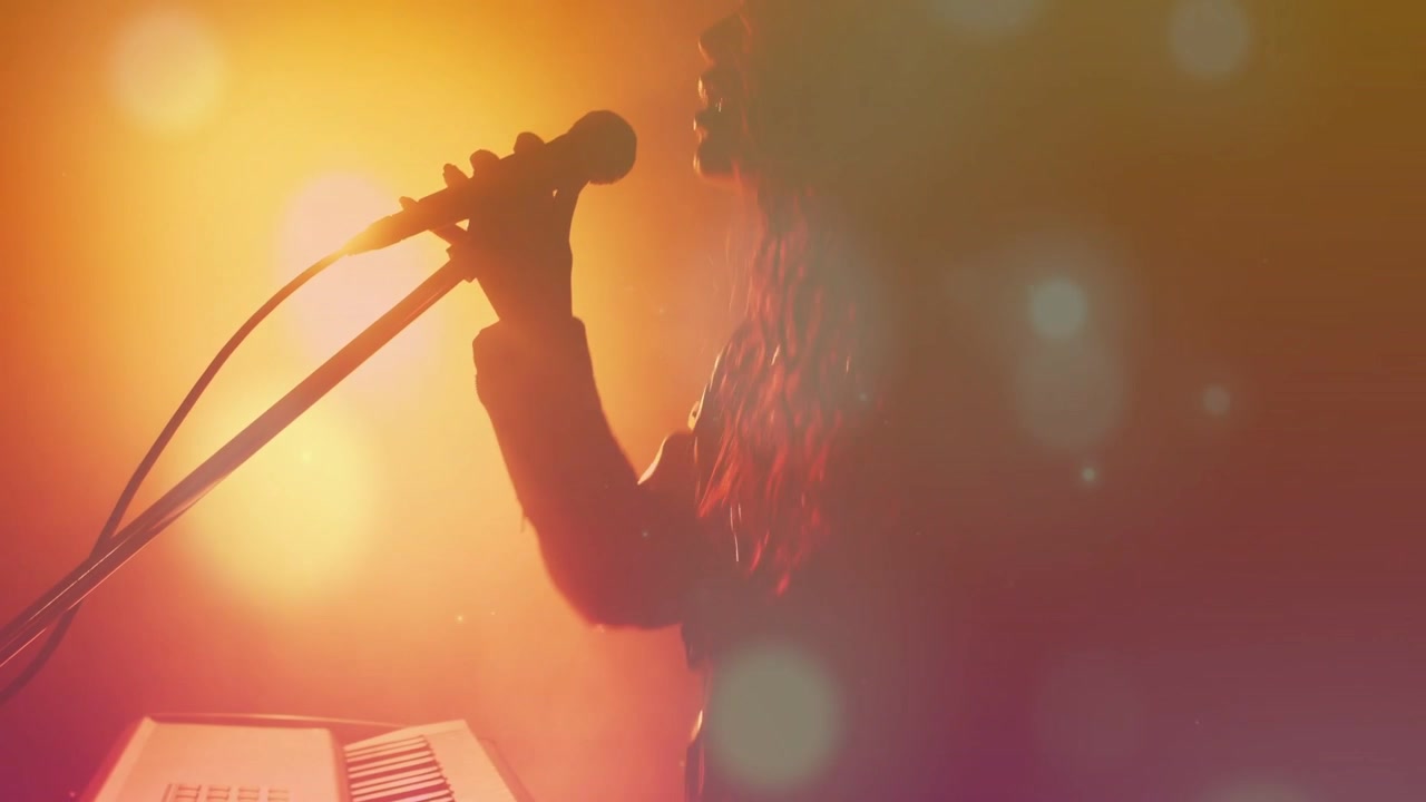Video vertikal: Artis wanita memainkan synth lalu meraih mikrofon, memulai pertunjukan di tengah kabut suar lensa.