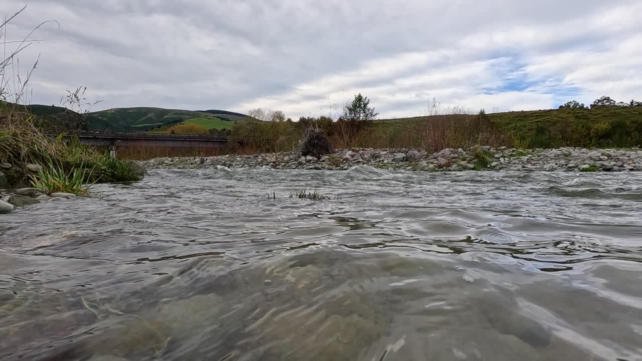 A serene river scene with gentle ripples and lush greenery under a cloudy sky, captured in Akaroa, New Zealand