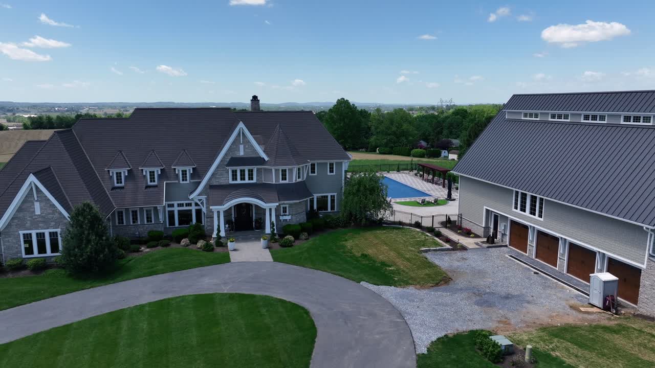Aerial view of luxurious countryside estate with large mansion, detached garage, circular driveway, manicured lawn and backyard pool. Surrounded by open fields and scenic landscape. Pennsylvania, USA.