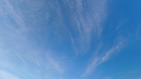 High-wispy-cirrus-clouds-move-slowly-across-empty-blue-sky,-background