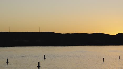 Speed-buoys-bob-in-even-and-calm-waters-of-Lake-Havasu-as-the-sun-sets-over-the-mountain-hilside-in-the-distance