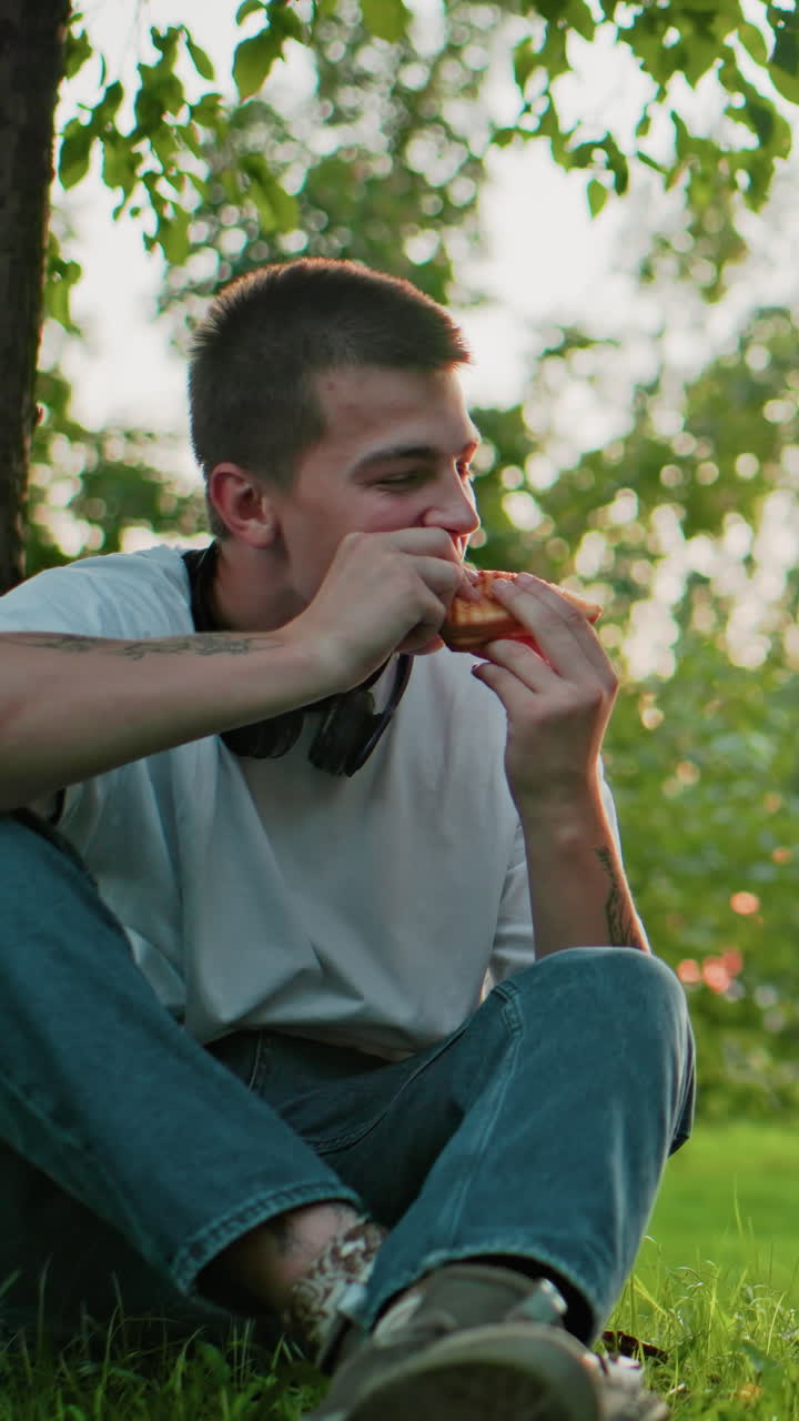 niño y niña sentados al aire libre con una computadora portátil delante, haciendo un brindis con pan en la mano, disfrutando de una comida juntos bajo la sombra de un árbol, la luz del sol filtrándose a través de las hojas en el fondo