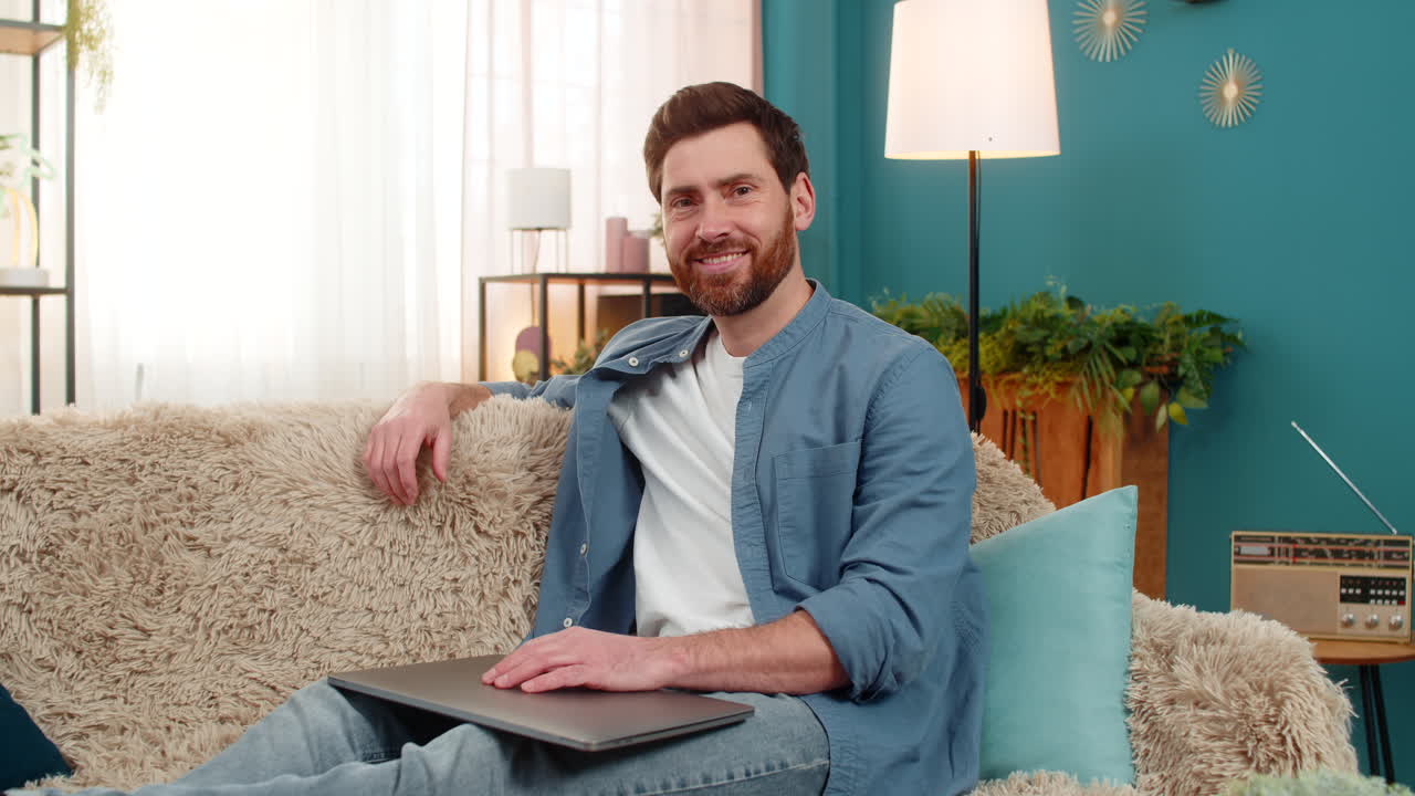 Young man smiling with satisfaction while closing laptop feeling happy and accomplished after work