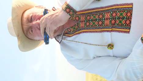 a lonely talented elderly man in ukrainian national clothes plays the harmonica a lonely talented elderly man in ukrainian national clothes plays the mouth organ harmonica sits in the middle of the field grandfather in an embroidered shirt