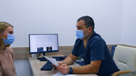 mid-aged dark-haired male doctor in mask giving test analyses to his female patient. obstetrician asking question and receiving negative reply.