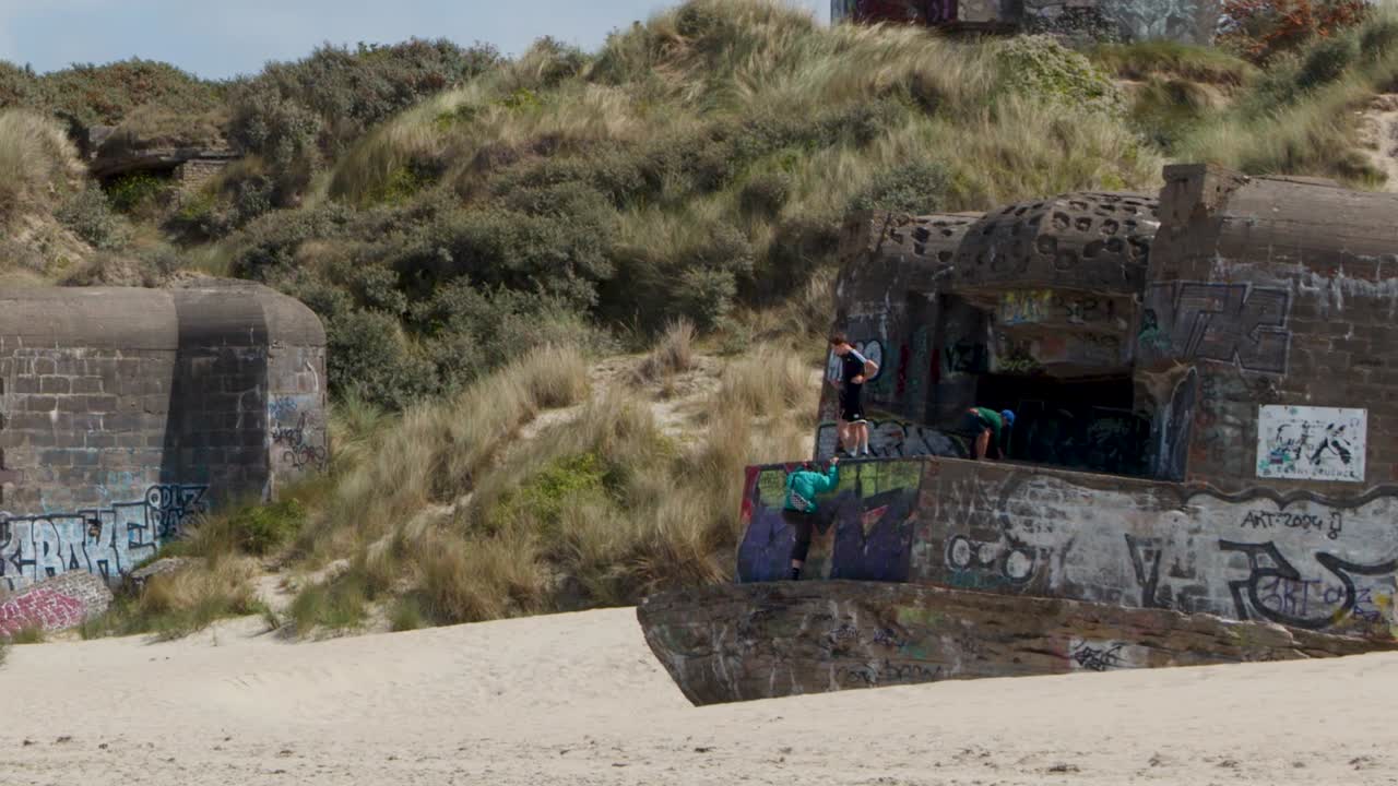 Statisk halvbild av en övergiven betongbunker med färgglad gatukonst på kustdyner