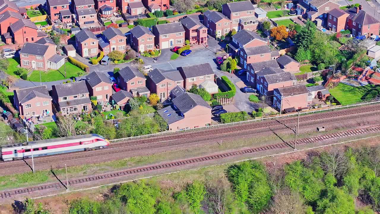 Aerial view of a commercial train passing by a residential area in Wakefield city, West Yorkshire, England. Showing typical British brick housing and lush green gardens, under a clear sunny day.
