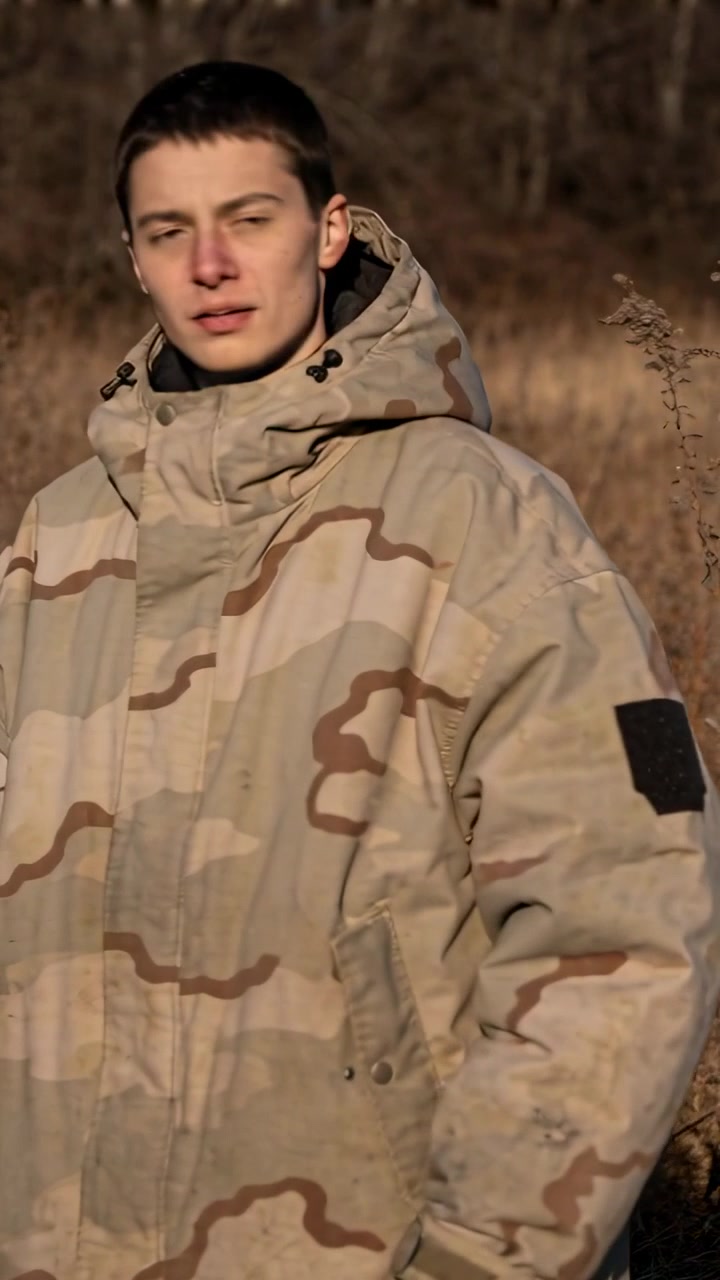 Vertical video: Squinting from bright sun, man turning head to check field in tan camo parka