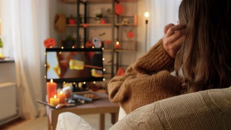 a woman watches a movie with friends during a cozy halloween night in her living room.