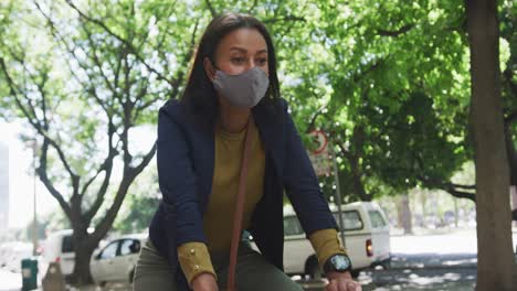 African-american-woman-wearing-face-mask-riding-bicycle-in-street