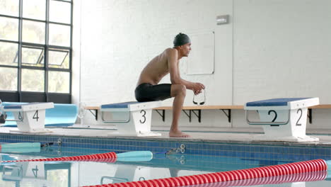 young biracial male athlete swimmer prepares to dive at an indoor pool