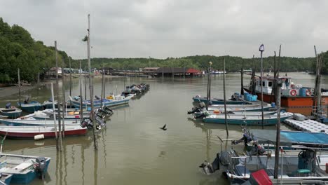 Calm-Fishing-Pier-with-Small-Boats-nestled-in-the-Mangrove-Forest-Cloudy-Day,-Strait-of-Johor-Malaysia-Singapore-Border-Fishing-Industry-in-the-Johor-Strait