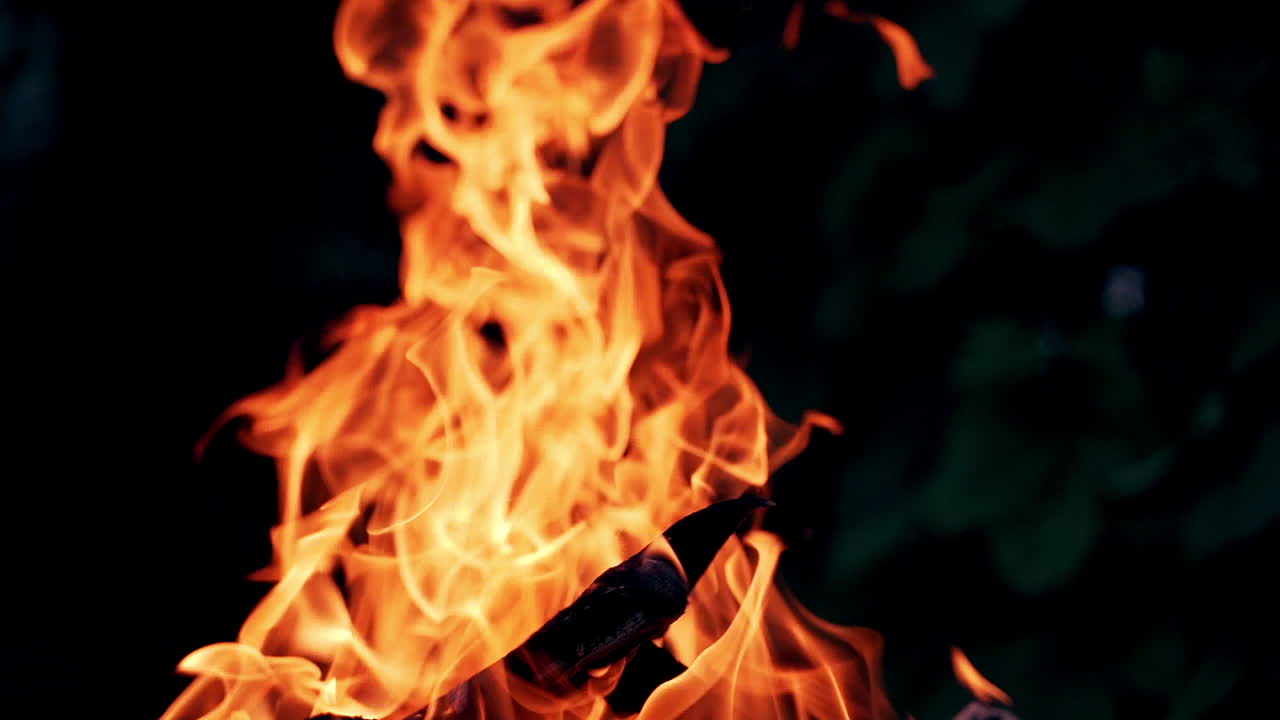 Bright flame from smoldered logs on dark background. Wood burning slowly with orange fire flame. Close-up.