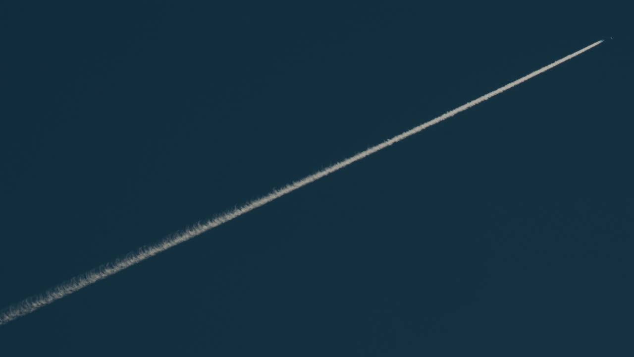 Airplane flying high above leaving long contrails in a clear blue sky