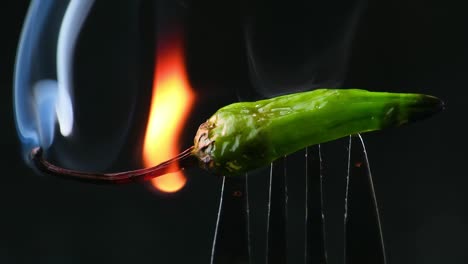 Brennende-Scharfe,-Scharfe-Grüne-Chilischote-Auf-Einer-Gabel-In-Flammen-Auf-Schwarzem-Hintergrund