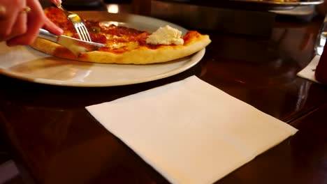 a female cutting a pizza with a fork and knife in a pub