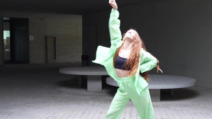 A woman is energetically dancing outdoors in a green outfit showcasing vibrant movements