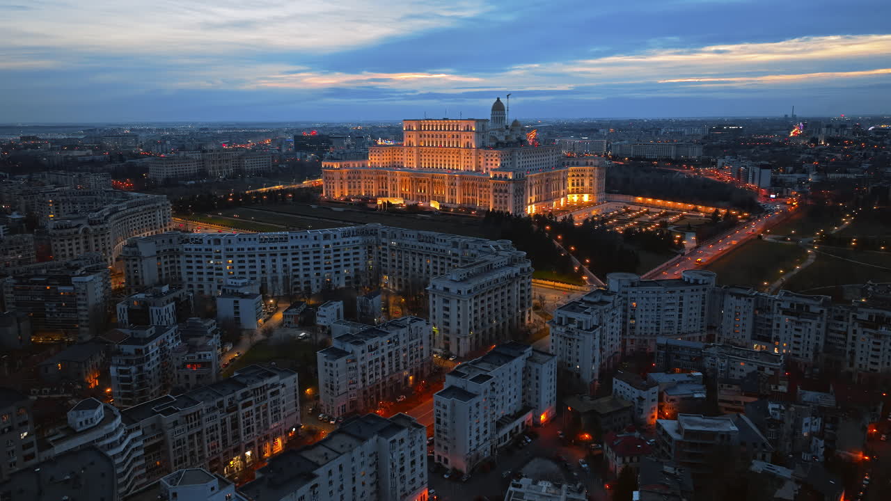 Aerial drone view of illuminated Palace of the Parliament in Bucharest downtown in the evening. Multiple districts around. Romania