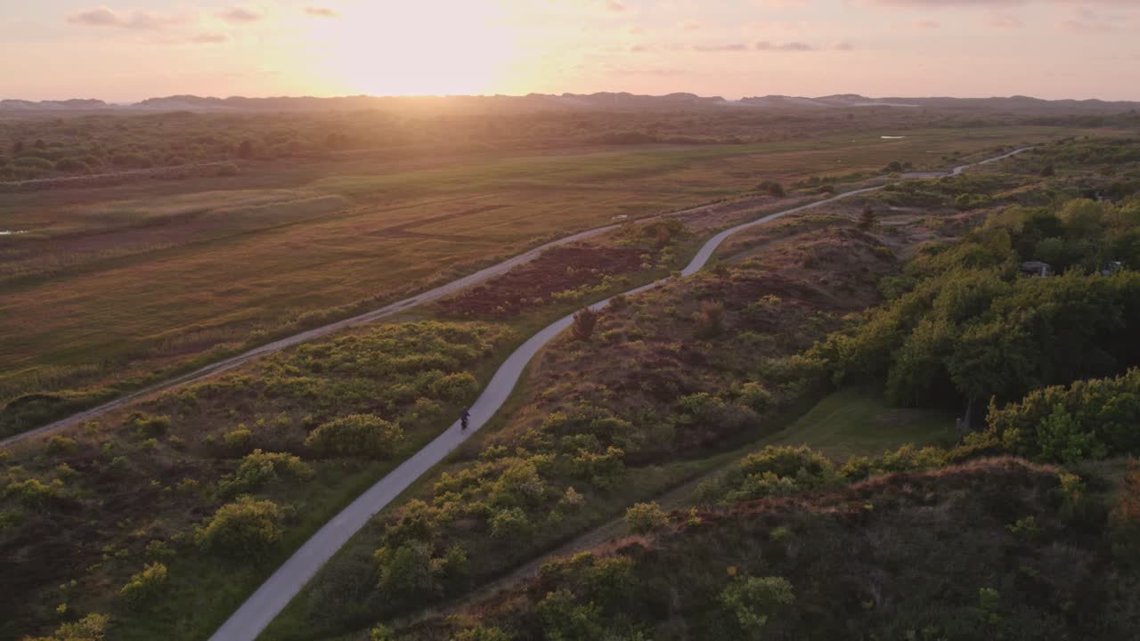 hombre está en bicicleta en el camino de grava en la isla de terschelling durante la puesta de sol, antena
