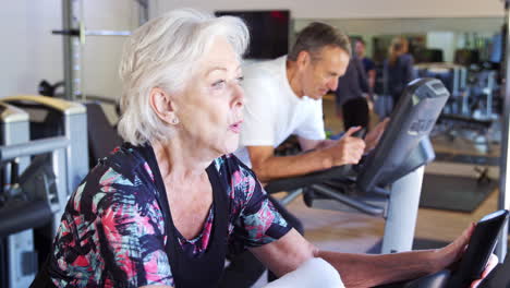 Pareja-Senior-Activa-Haciendo-Ejercicio-En-Máquinas-De-Ciclismo-En-El-Gimnasio