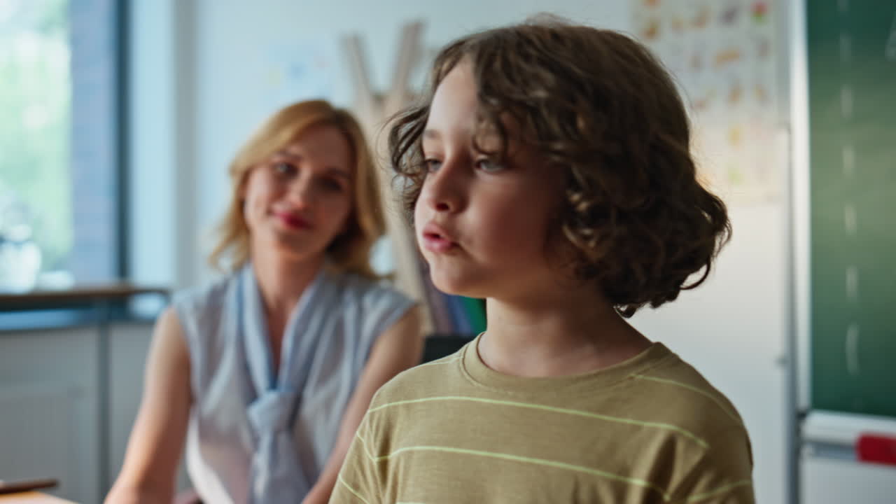 Teacher guiding young boy at classroom lesson closeup. Woman tutor asking pupil