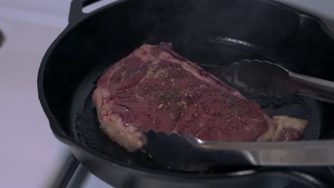 dinner steak cooked on a cast-iron skillet ready to flip over with stainless steel tongs