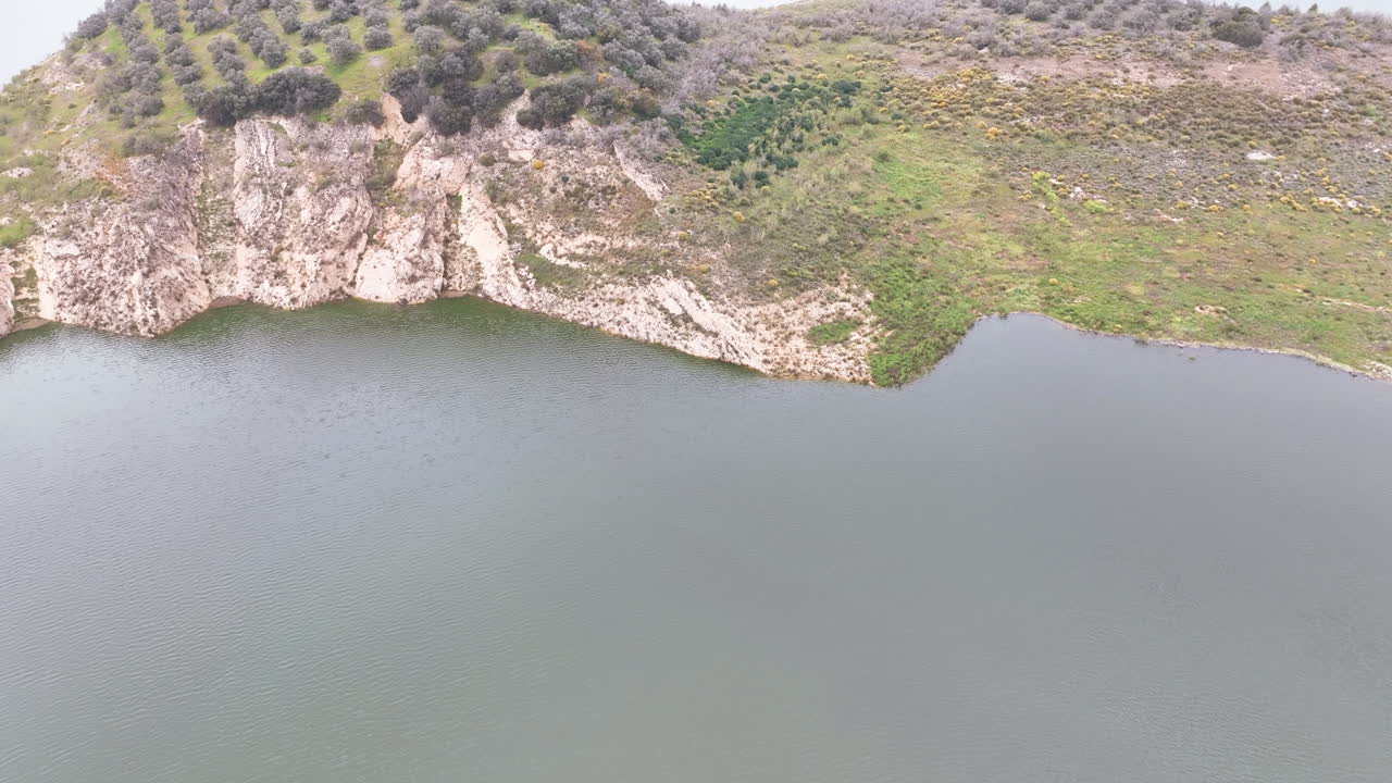 Autumn flight across Iznajar's dark green lake towards cliff side olive grove