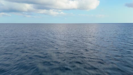 aerial pullback above ocean water surface texture with calm peaceful clouds