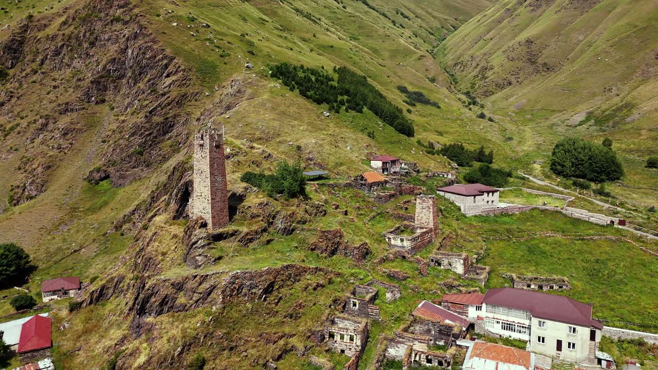 Historic tower in Kazbegi valley rural rugged valley. Drone aerial fly through t old stone buildings in rocky village landscape