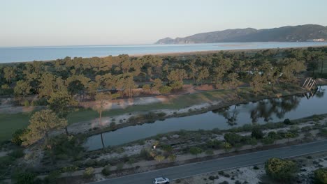 Vista-Aérea-De-Troia-Golf,-Enclavada-Entre-El-Estuario-Del-Sado-Y-La-Majestuosa-Montaña-Arrábida,-Iluminada-Por-Un-Radiante-Amanecer