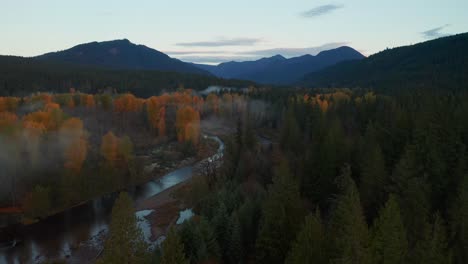 Stunning-Aerial-in-Pacific-Northwest,-Showcasing-Opposites-on-Each-River-Shore:-Green-Pines-and-Autumn-Colored-Trees