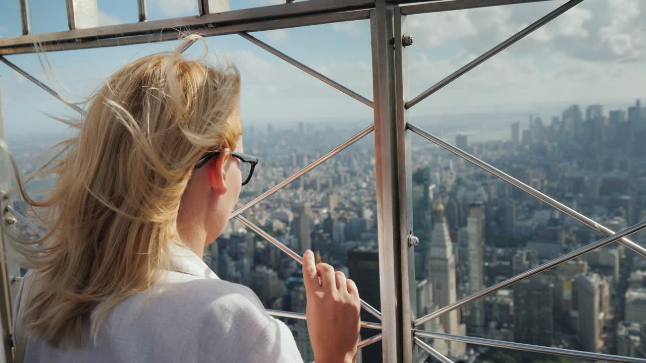 한 여성이 울타리에 서 있는 맨해튼 비즈니스 지구의 아름다운 전망을 내려다보고 있습니다.