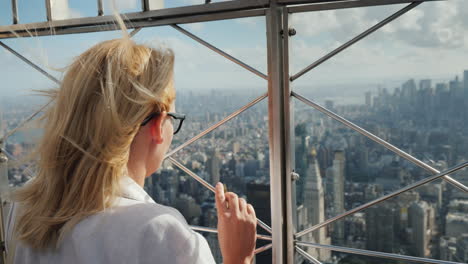 a woman looks down at a beautiful view of the business district of manhattan it stands at the fence