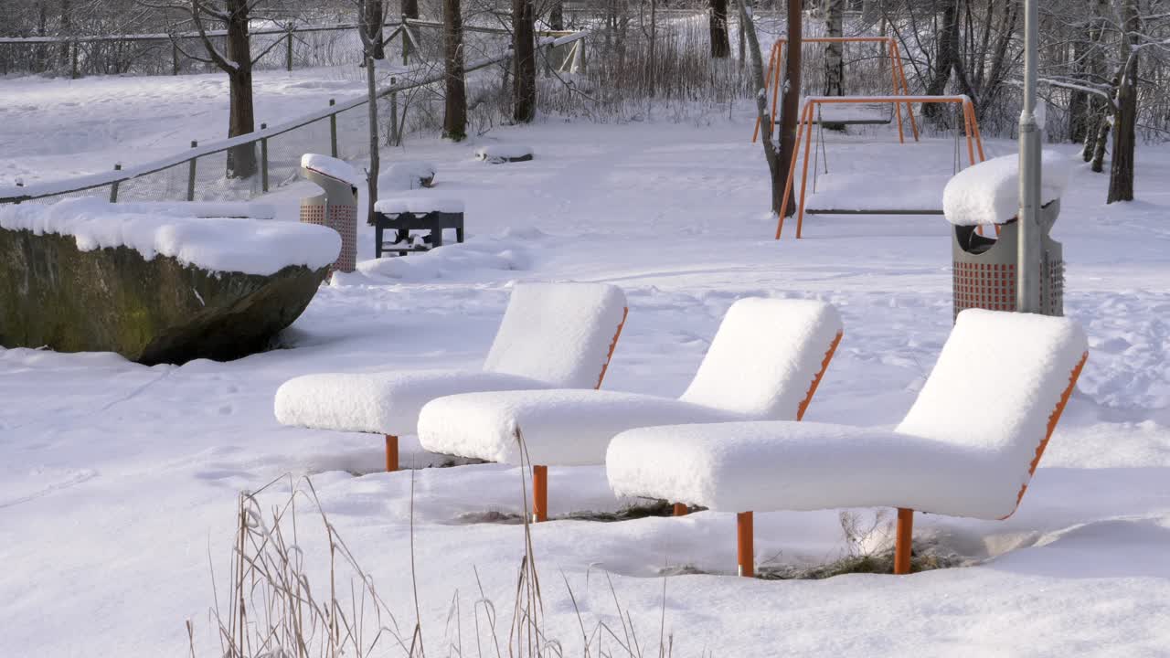 Tjockt snötäcke täcker vilande solstolar i allmän park i Sverige