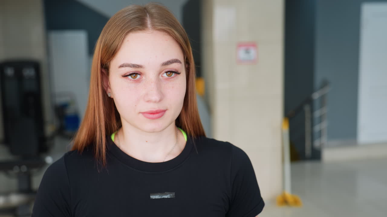 focused young woman exercising in spacious gym wearing black athletic top with blur view of person working out in background and sleek modern gym design featuring neutral tones and lighting