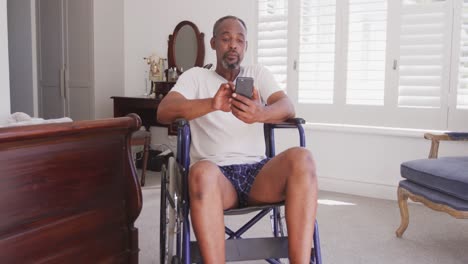 Senior-African-American-man-on-a-wheelchair,-using-his-phone,-smiling-at-home