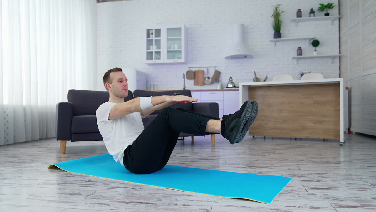 Strong man on quarantine working out in home. Young athletic healthy male training indoors while sitting at the mat
