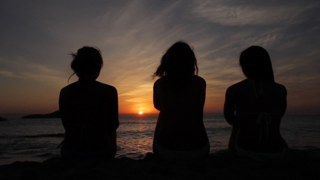 Silhouette of three friends at sea in golden and beautiful sunset. . Young women on holidays summer evening. Happy people watching the sunset, Ibiza Cafe del Mar, Spain