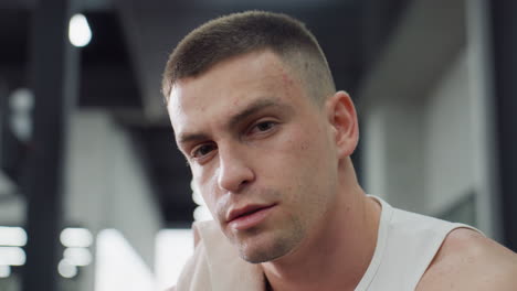 portrait of gym goer sits on weight bench with towel draped over shoulder exhaling in relief after intense chest press workout under gym lighting showing focused calm expression during recovery