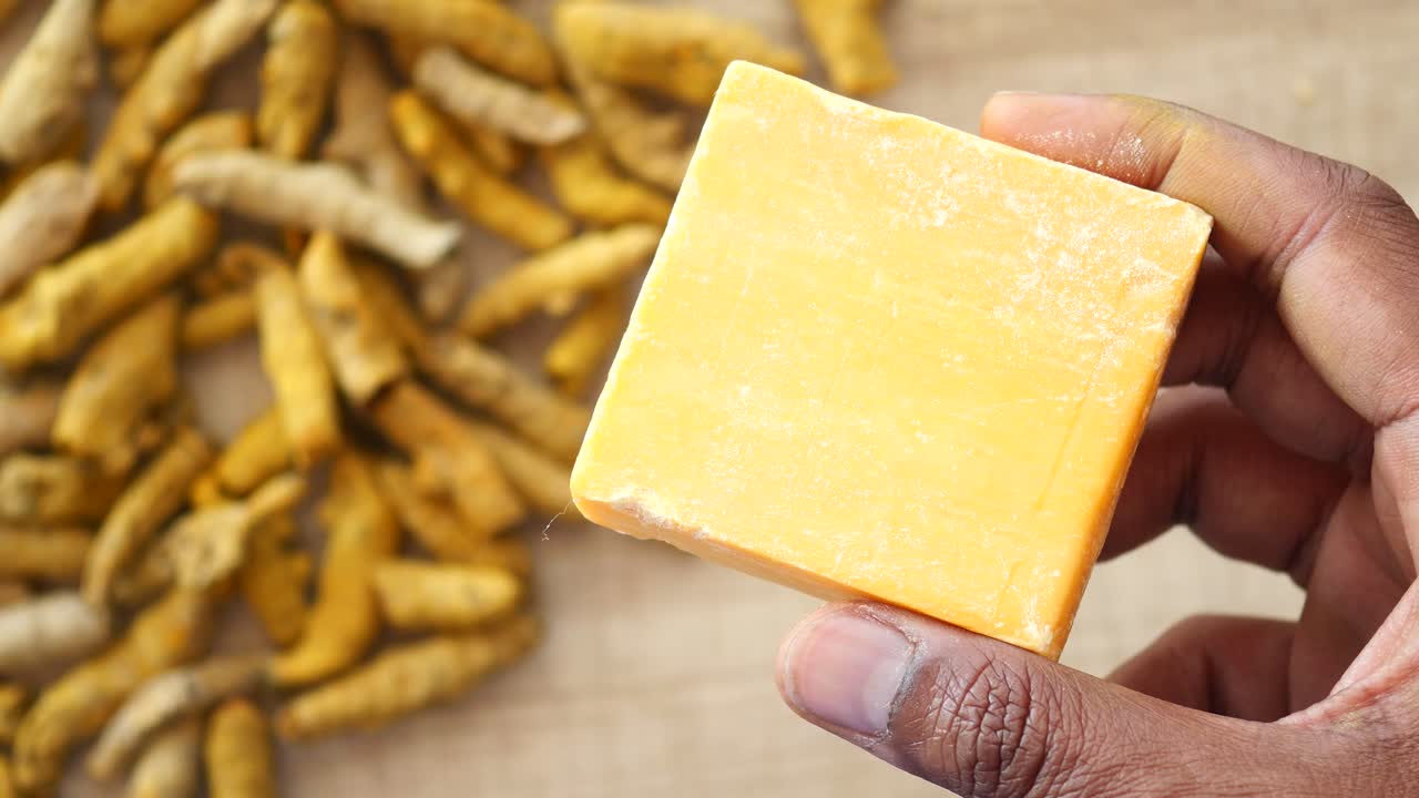 Hand holding a block of turmeric soap with dried turmeric roots in the background