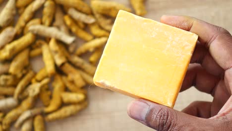 hand holding a block of turmeric soap with dried turmeric roots in the background