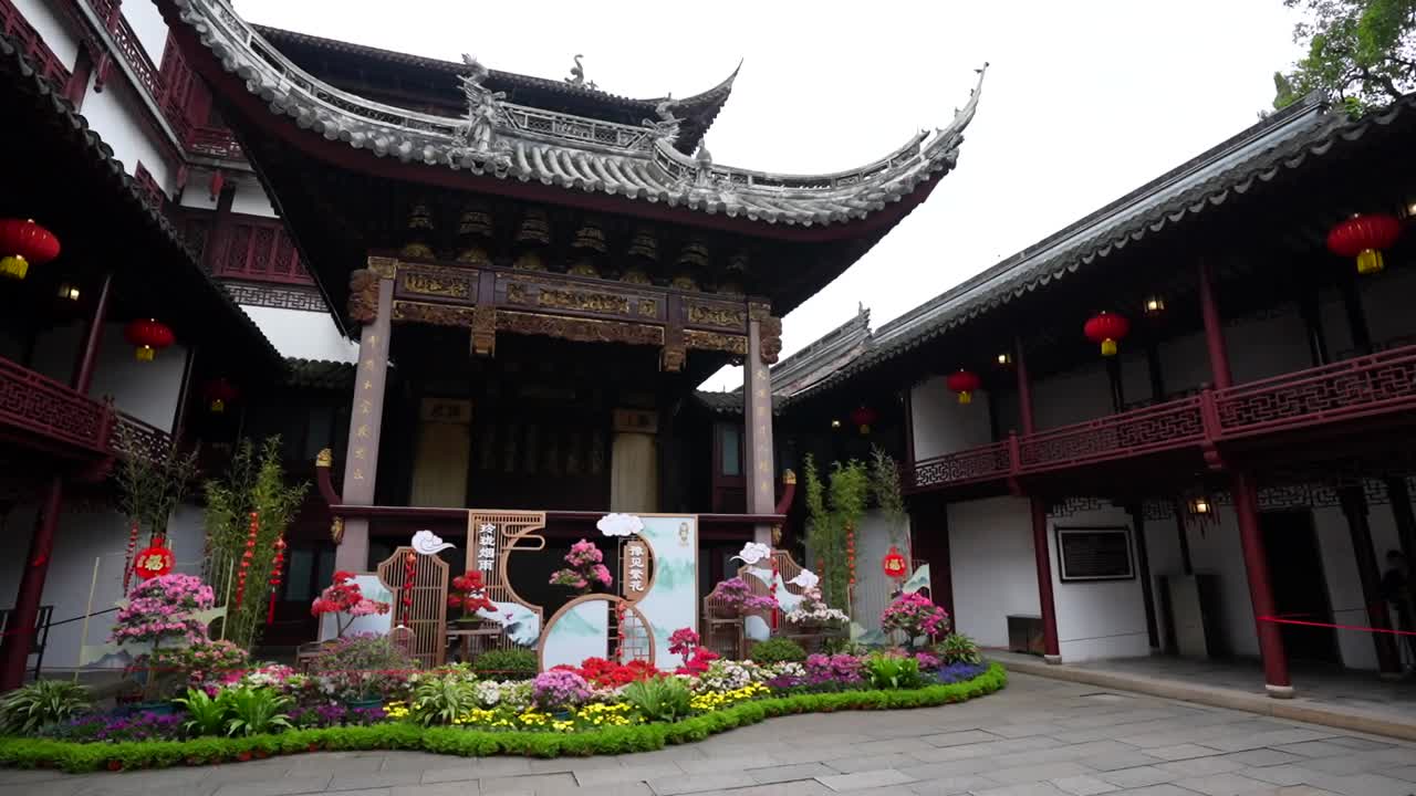 Panning left to a pagoda framed by flowers and balconies with red lanterns at Yuyuan Garden in Shanghai, China