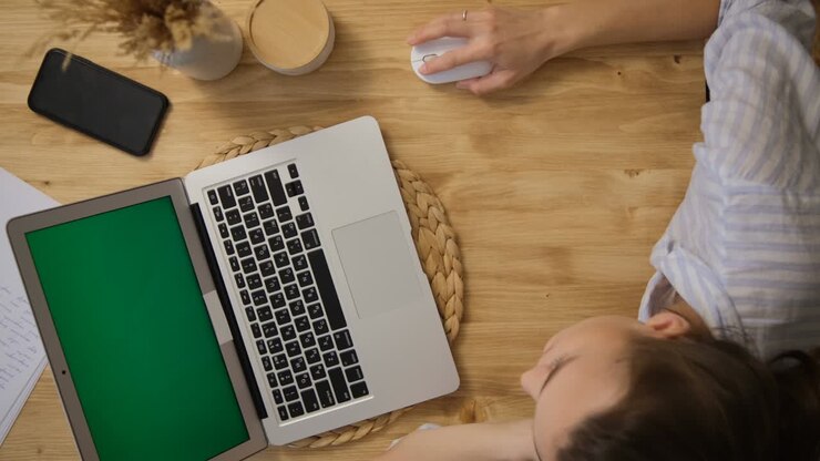Schermo del computer verde. La ragazza è sdraiata al tavolo e studia, lavora da remoto. Una ragazza con un top del pigiama a righe. Vista dall'alto