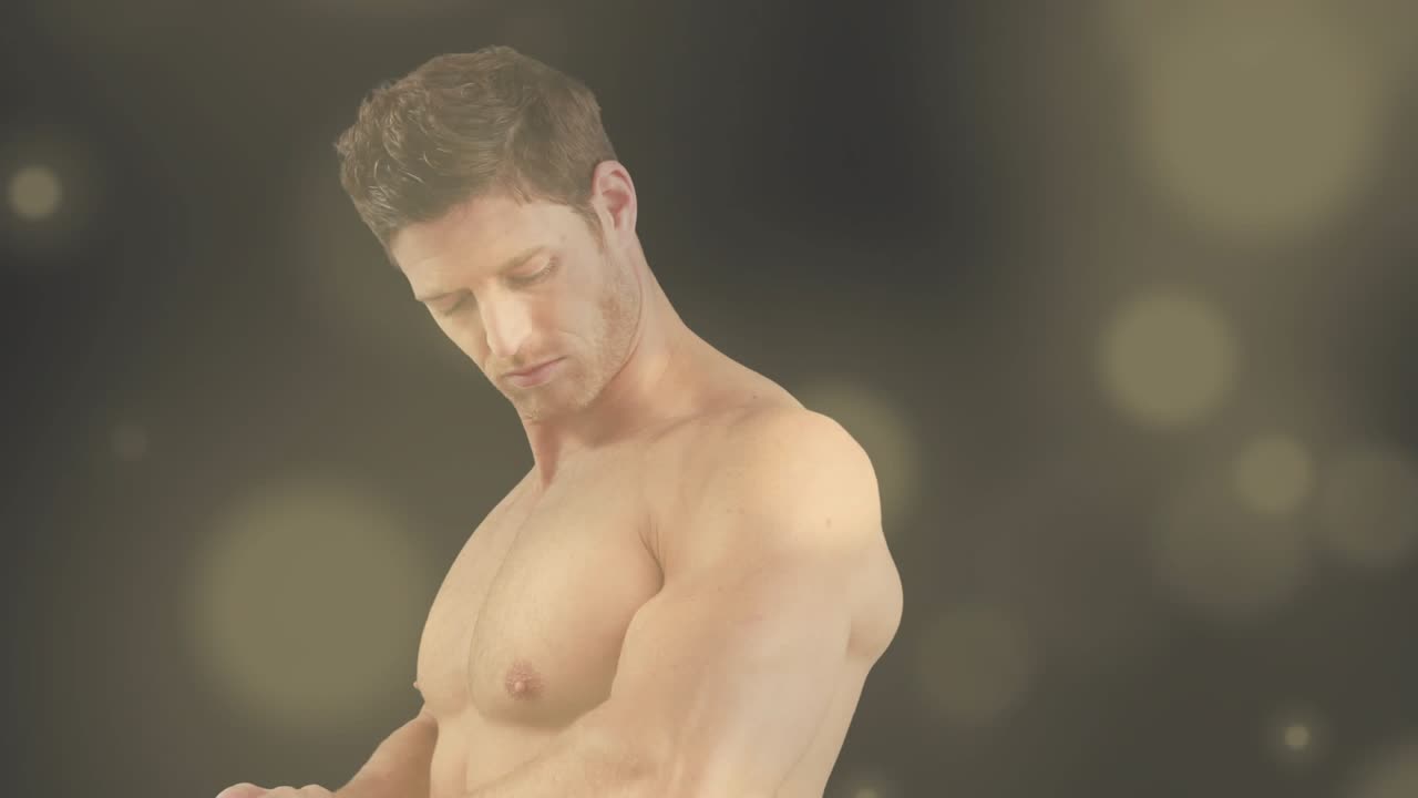 Male model shifting weight and rotating torso in studio, showing muscles with warm bokeh lighting