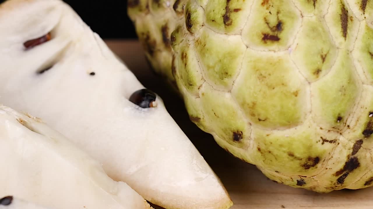 Detailed view of custard apple skin and white slices with seeds on a dark background.